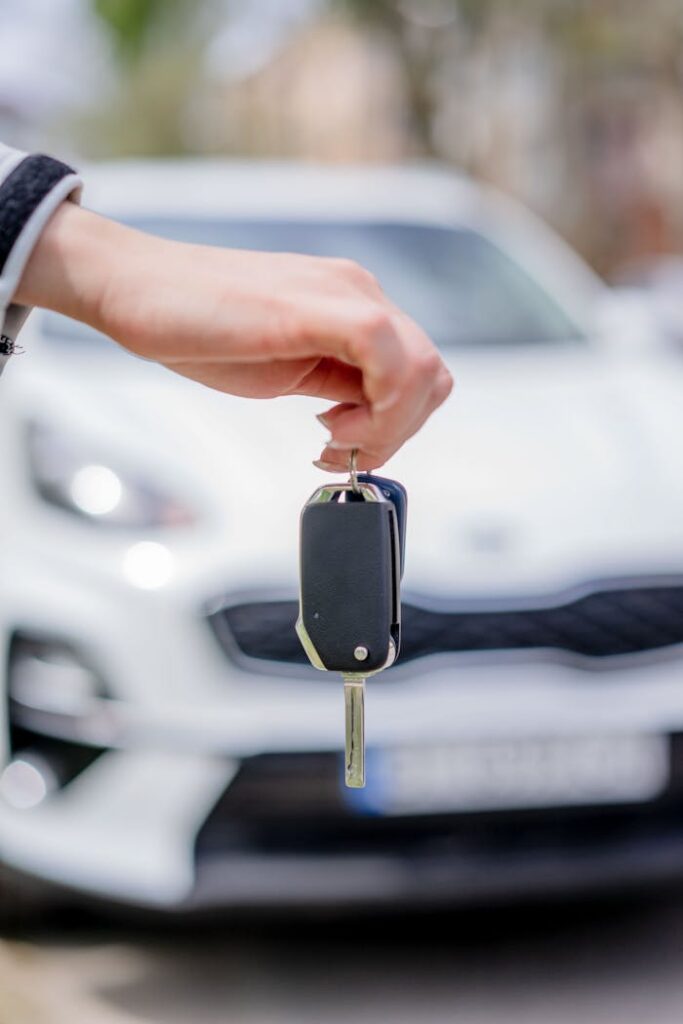 pexels photo 12969398 Close-up of a hand holding a car key, with a white car in the background outdoors.