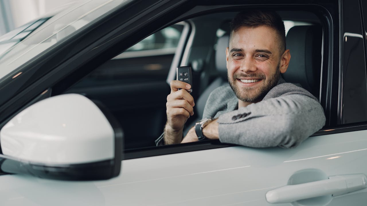 Jak sprawdzić samochód przed zakupem? O czym warto pamiętać? Happy young man holding car keys inside a vehicle. Perfect image for car rental or sales.